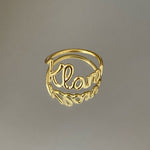 A gold-colored personalized ring with the name 'Klara' written on it, displayed against a gray background.