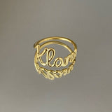 A gold-colored personalized ring with the name 'Klara' written on it, displayed against a gray background.