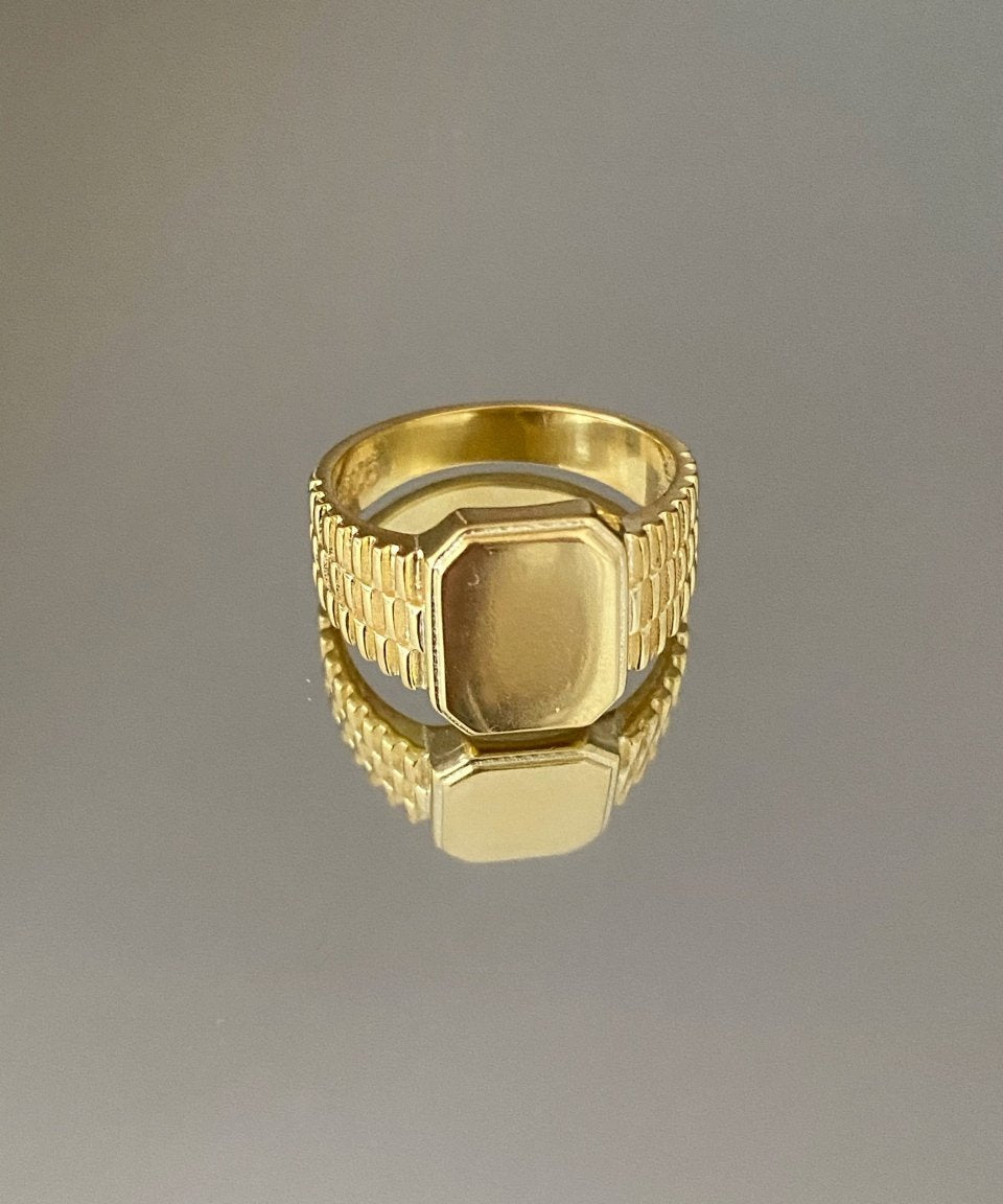 A gold-colored signet ring with engraved detailing and a polished finish.