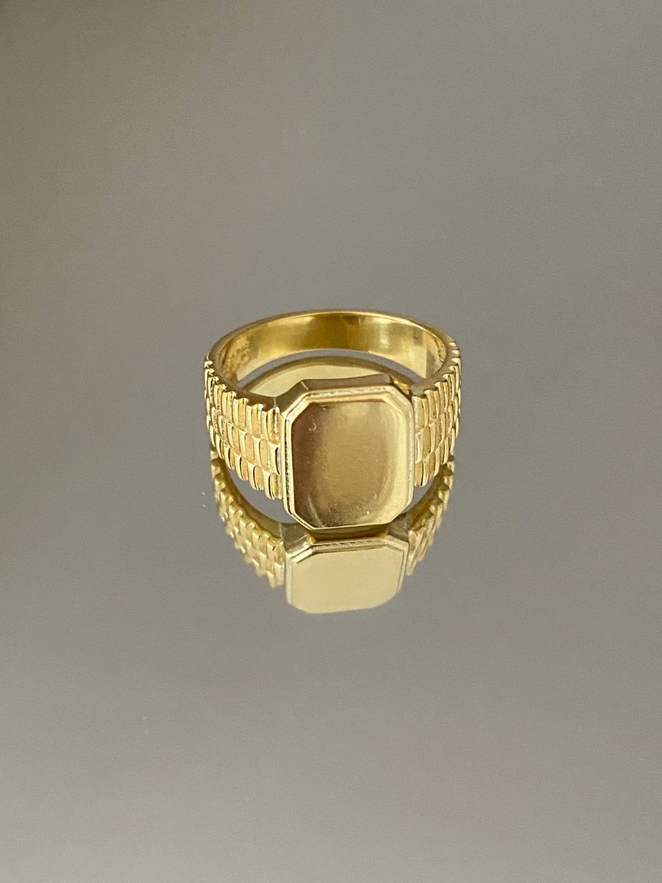 A gold-colored signet ring with engraved detailing and a polished finish.
