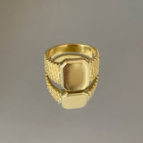 A gold-colored signet ring with engraved detailing and a polished finish.