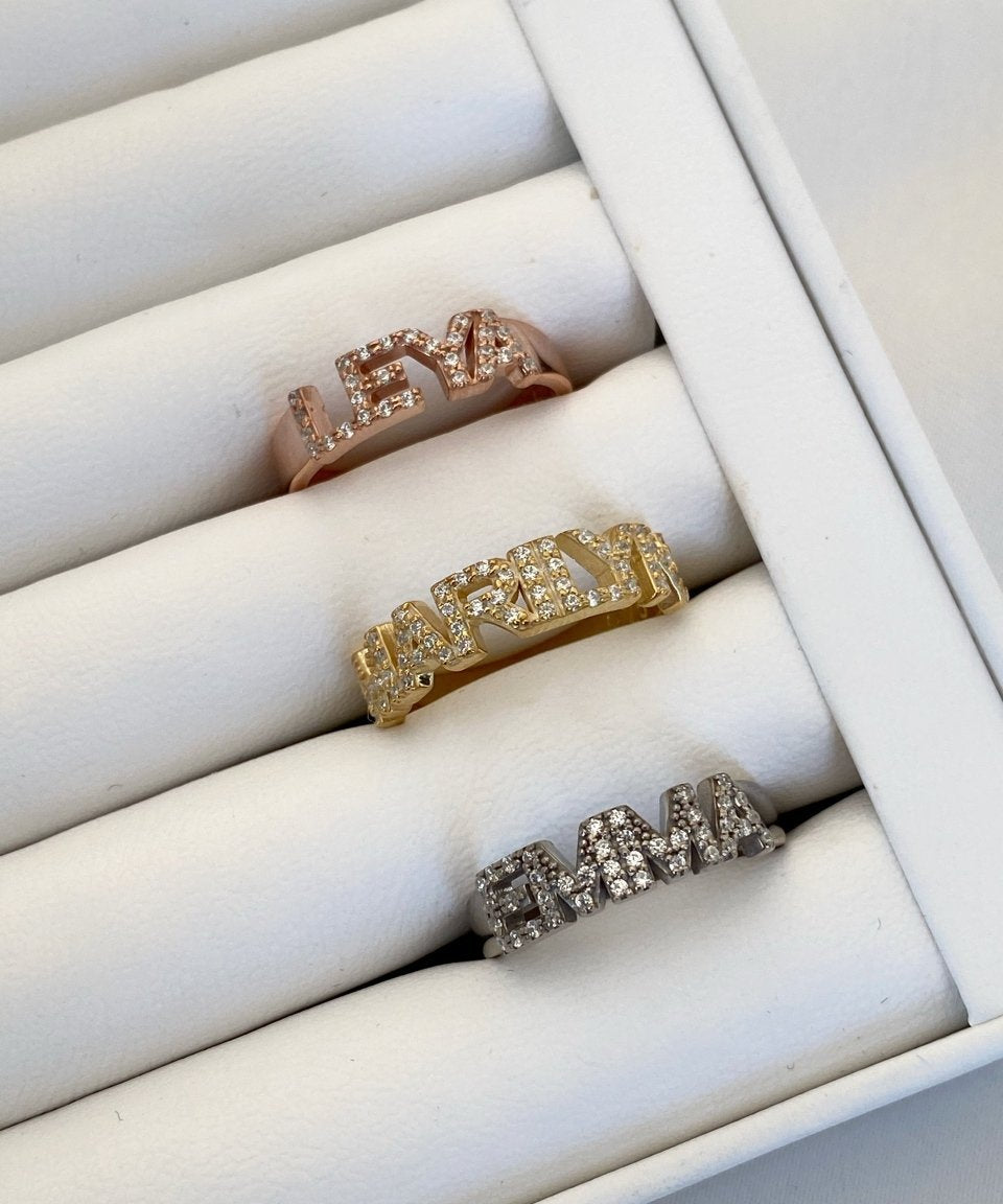 A set of silver rings with varying designs, displayed in a box, with one ring featuring a custom stone word inscription.