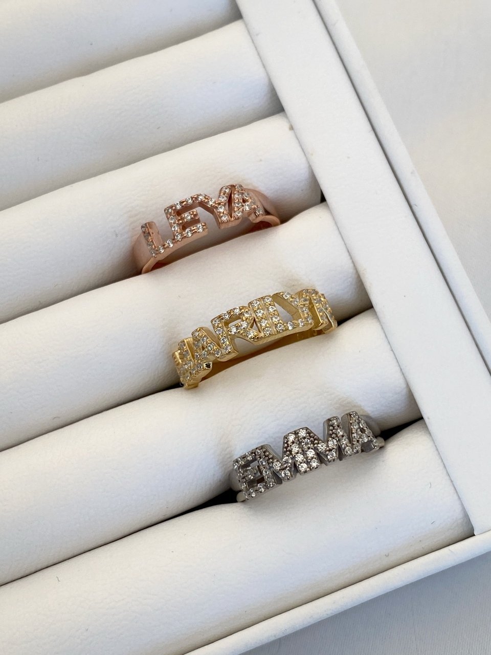 A set of silver rings with varying designs, displayed in a box, with one ring featuring a custom stone word inscription.