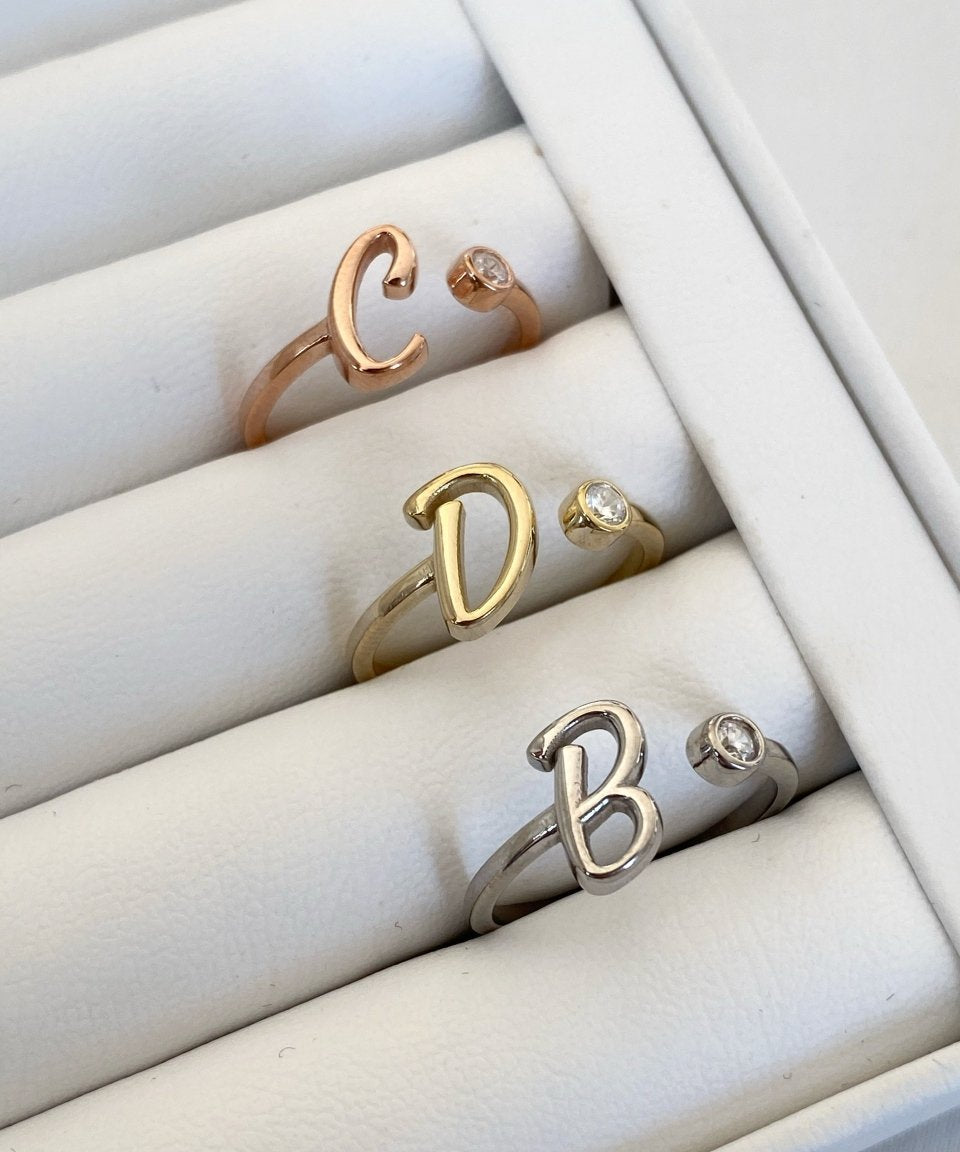 A collection of silver rings with letter details, displayed in a box. The letters visible are 'C', 'D', and 'B'.