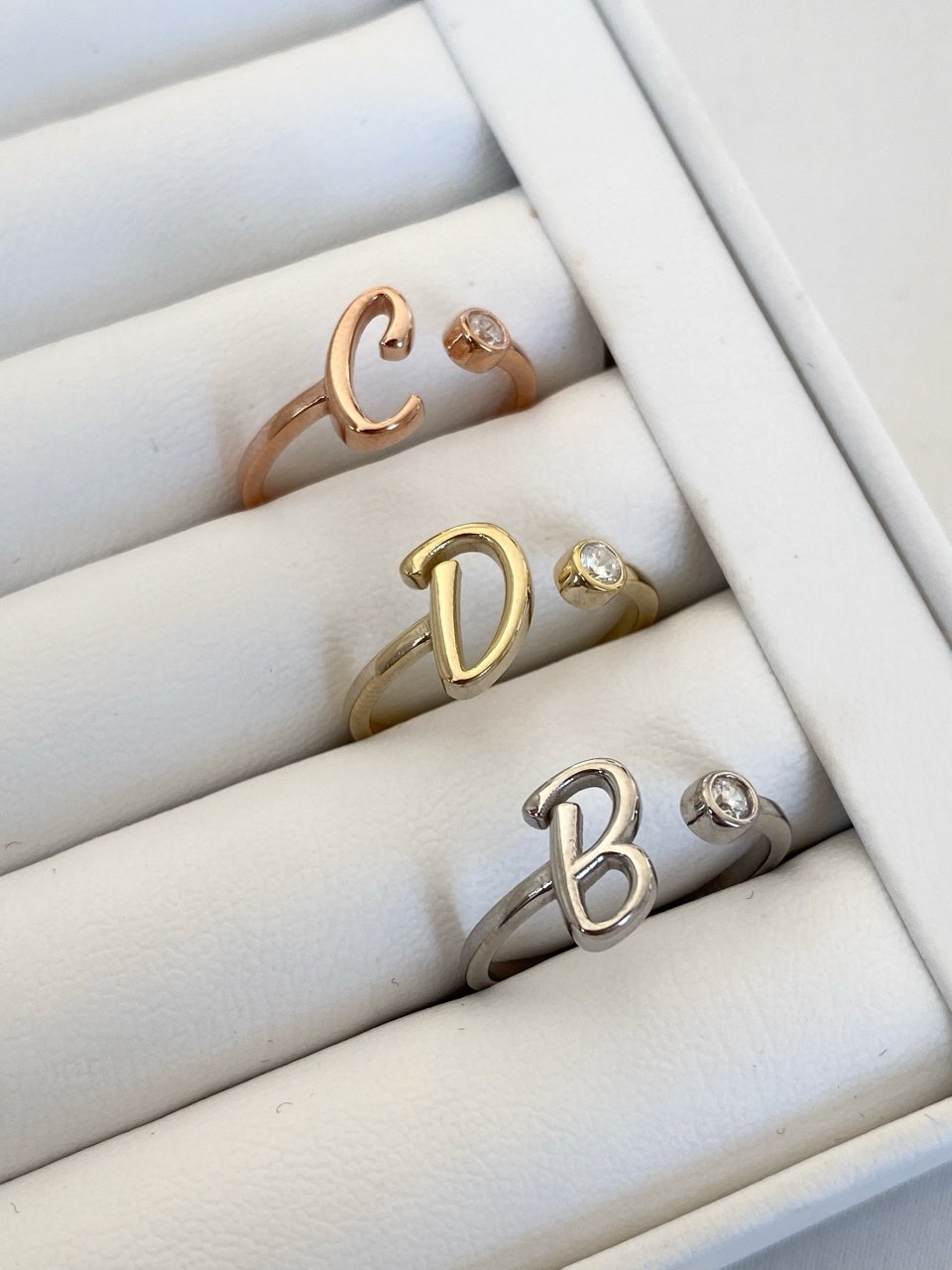 A collection of silver rings with letter details, displayed in a box. The letters visible are 'C', 'D', and 'B'.