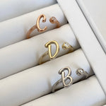 A collection of silver rings with letter details, displayed in a box. The letters visible are 'C', 'D', and 'B'.