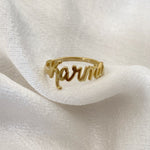 A gold-colored custom ring with the name 'Karma' written on it, displayed on a white fabric surface.